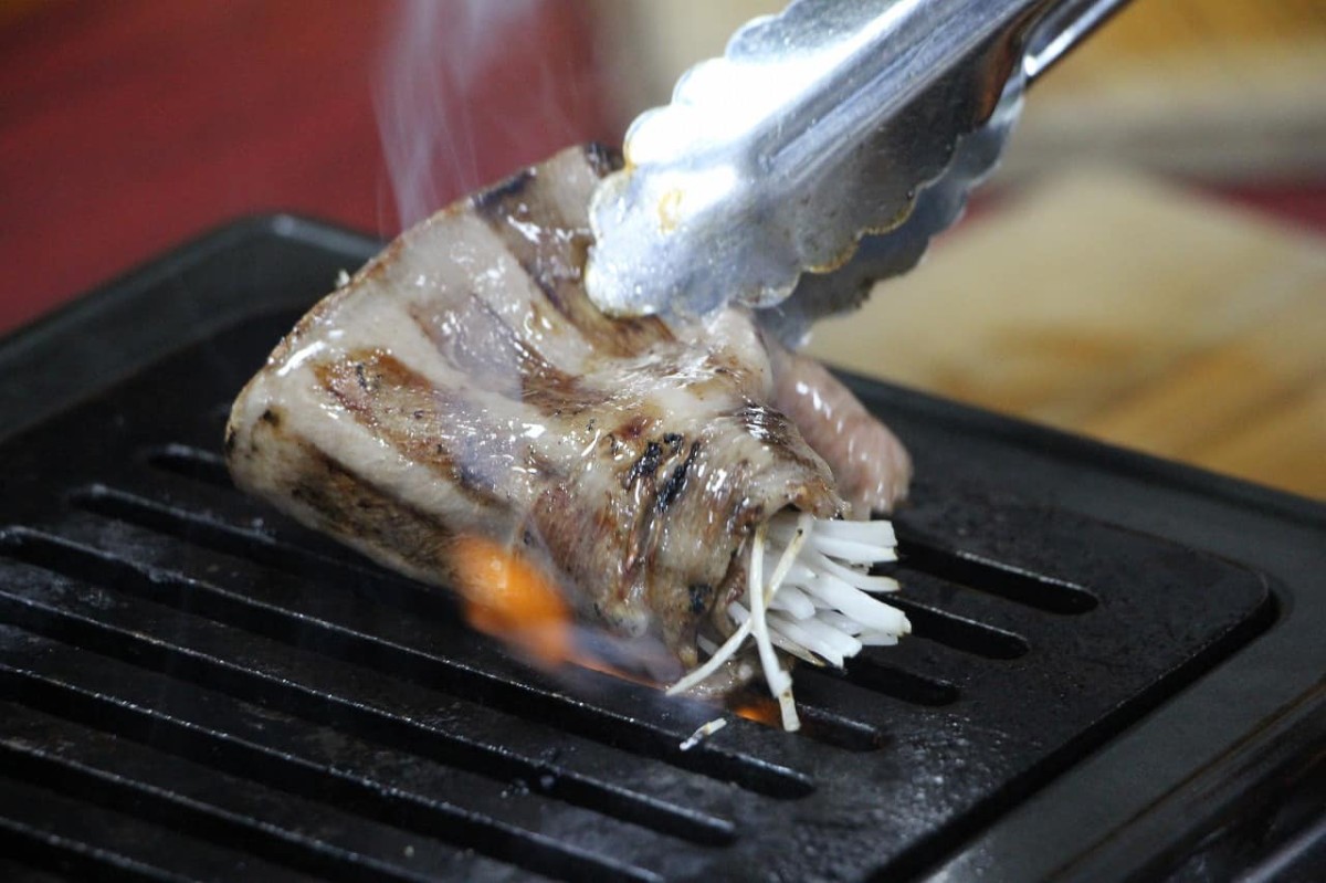 島根県松江市伊勢宮にある『叉鬼の焼肉酒場』で提供している「和牛たてわりタン」で白ネギを包む様子